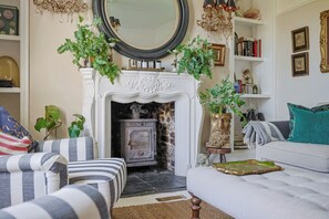 Ein Wohnzimmer mit Kamin, einer Couch, einem gestreiften Sessel und einem Bücherregal.