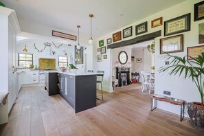 Eine geräumige Küche mit Kochinsel, ein Essbereich mit Kamin sowie ein Wohnbereich mit großem Spiegel und Wandbildern.