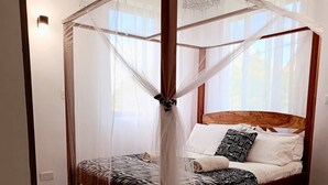 Nelipylväinen katosvuode, jossa on seeprankuvioinen peitto, valkoiset tyynyt ja mustavalkoinen kuviotyyny.