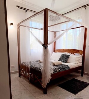 Una cama con dosel y cuatro columnas, con colcha de estampado de cebra, almohadas blancas y cojín con estampado blanco y negro.