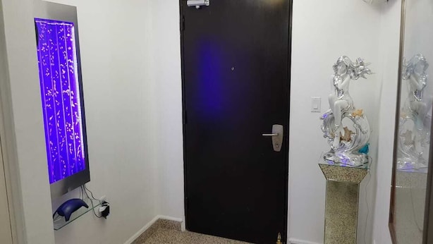 A hallway with a black door, a wall-mounted TV with a blue light, and a decorative silver statue on a pedestal. - Private  1-bedroom studio/efficiency safest location in Panama City: Walk to all (Panamá)