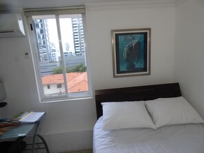 Ein Schlafzimmer mit Bett, Schreibtisch, Stuhl, Fenster und einem gerahmten Bild an der Wand.