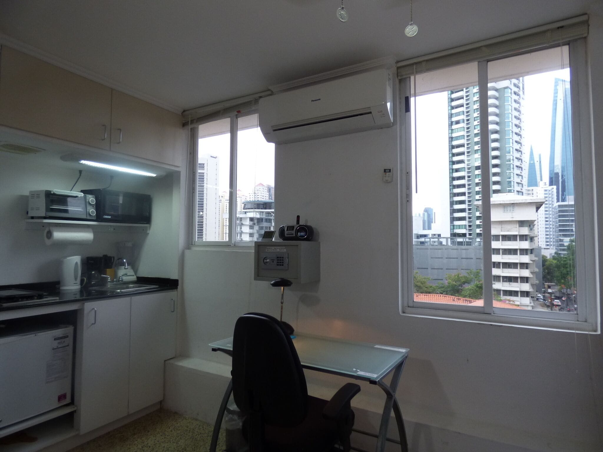 Ein kleines Büro mit Schreibtisch, Stuhl, Küchenzeile und großen Fenstern mit Blick auf die Stadt.