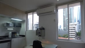A small office with a desk, chair, kitchenette, and large windows offering a city view. - Private  1-bedroom studio/efficiency safest location in Panama City: Walk to all (Panamá)