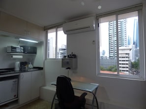 Ein kleines Büro mit Schreibtisch, Stuhl, Küchenzeile und großen Fenstern mit Blick auf die Stadt.