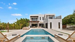 Una casa moderna de dos pisos con piscina, mobiliario exterior y un patio.