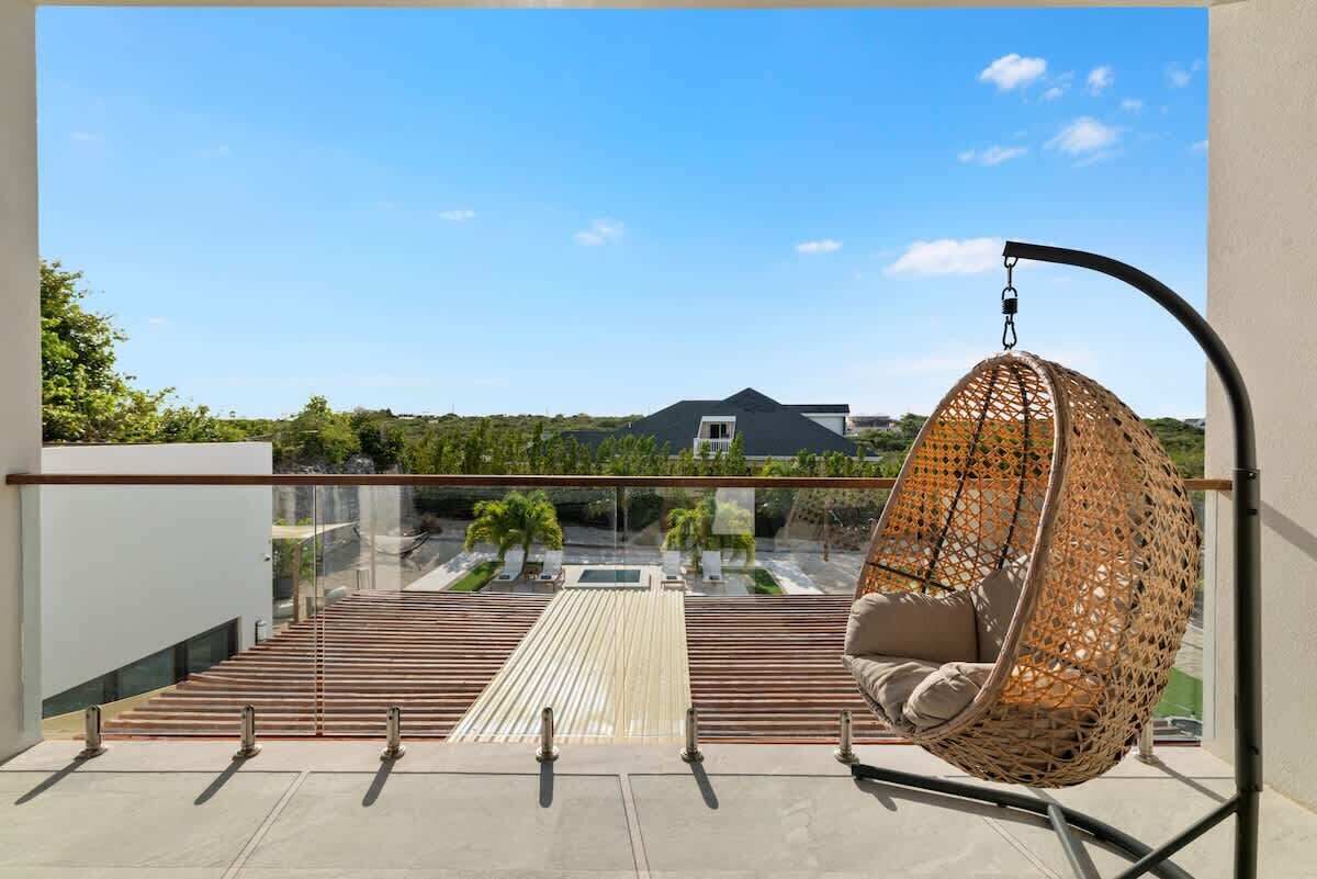 Een balkon met een hangstoel, glazen hekwerk en uitzicht op een woonwijk.