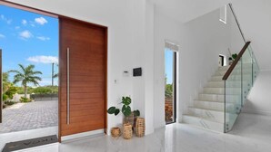 Un interior moderno con una puerta de madera, una escalera de cristal y vistas al exterior.