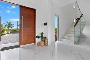 A modern interior with a wooden door, a glass staircase, and a view of the outdoors. - Long Bay Villa: Pool, Jacuzzi, Near Beach (Long Bay Hills)