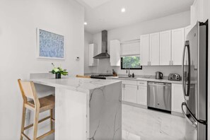 A modern kitchen with white cabinets, a marble island, stainless steel appliances, and a window with blinds. - Long Bay Villa: Pool, Jacuzzi, Near Beach (Long Bay Hills)