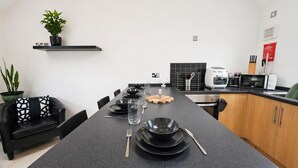 A modern kitchen with a black countertop, a dining table set with plates, bowls, and cutlery, a microwave, and a coffee maker.