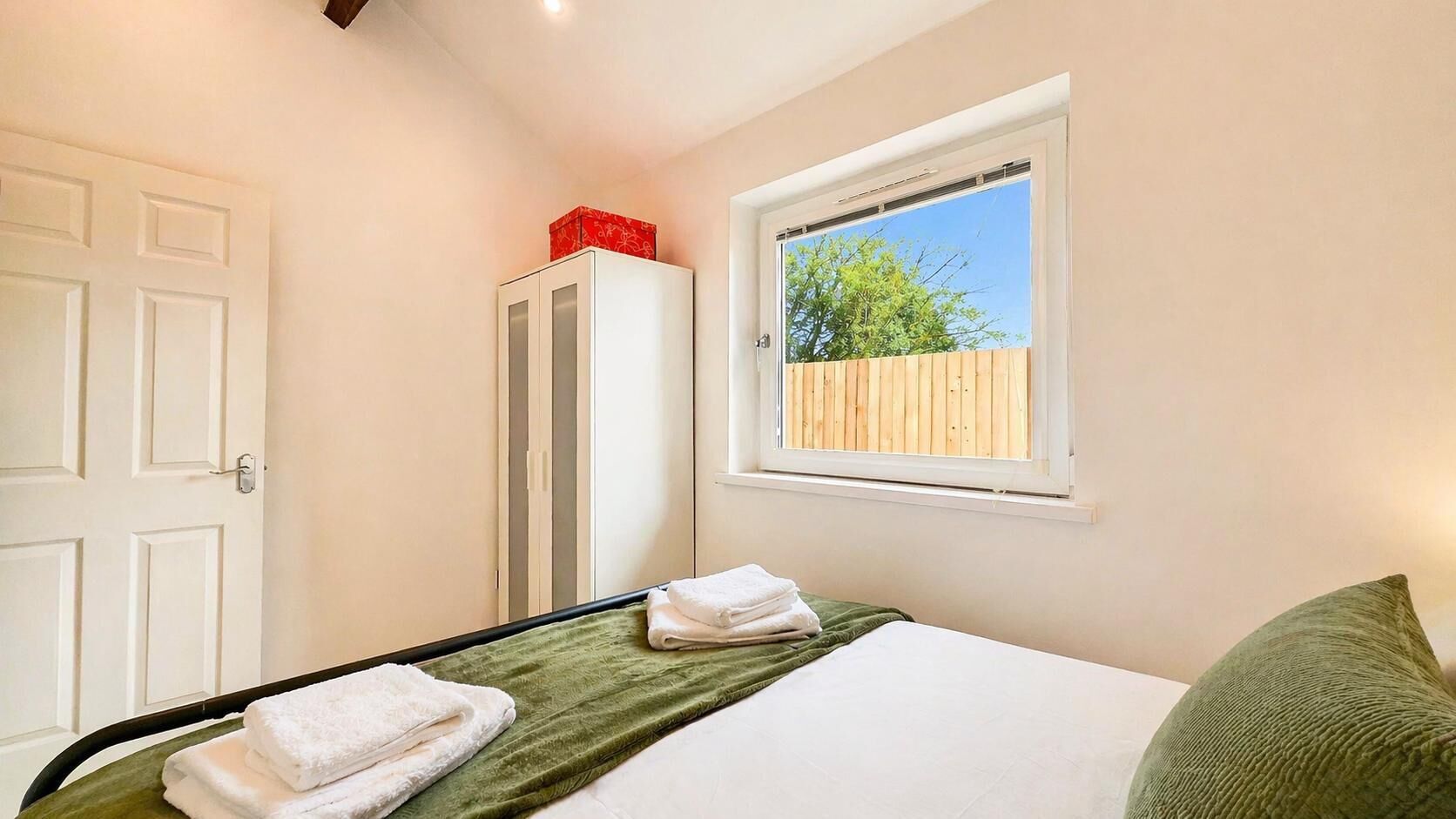 A bedroom with a bed, a window with a view, a wardrobe, and a door.