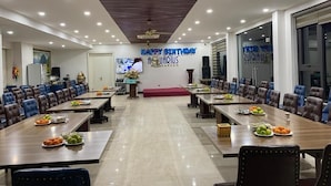 A conference room with multiple tables and chairs, a 'Happy Birthday Aquarius Garden' sign, and a television screen.
