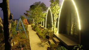 A pathway lined with trees and benches, leading to a building with illuminated arches.