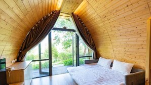 A cozy, wooden-paneled room with a bed, a desk, and a large window.