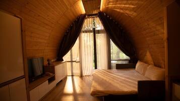 A cozy room with a sloped ceiling, a bed, a TV, and a window with curtains.