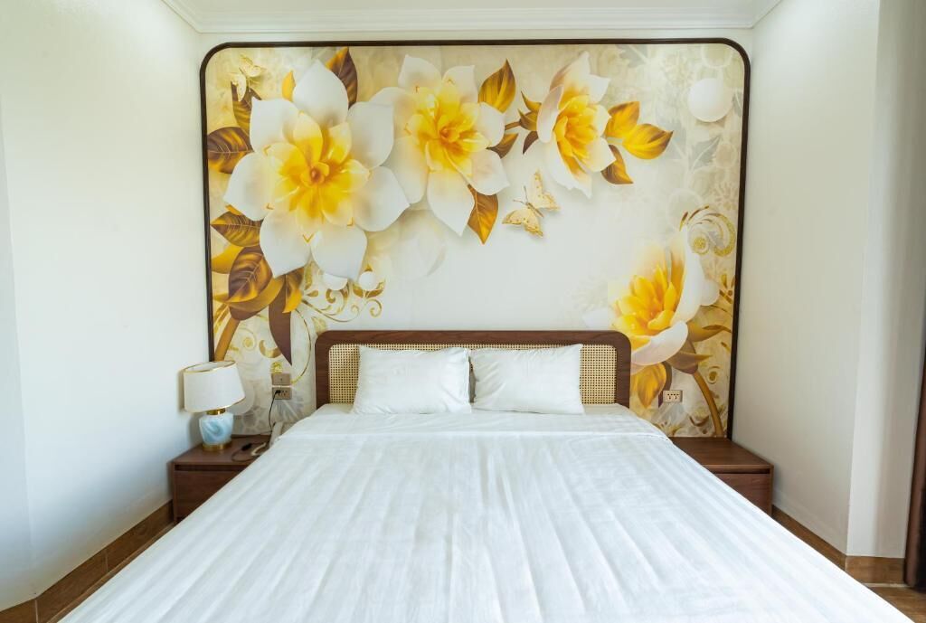 A bedroom with a large bed, a nightstand with a lamp, and a floral mural on the wall.