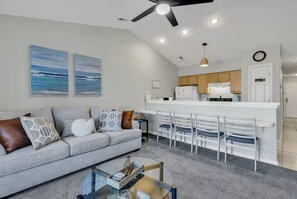 A modern living room with a sofa, coffee table, and a dining area with chairs. - Golf View River Oaks Condo Pool Myrtle Beach (Myrtle Beach)
