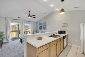 Una cocina moderna con una isla central, ventilador de techo, luces empotradas y vistas a una terraza exterior.