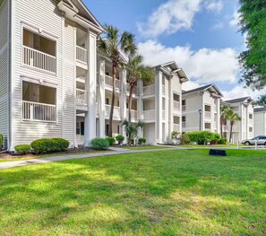 A row of white multi-story buildings with balconies, surrounded by well-maintained grass and palm trees. - Golf View River Oaks Condo Pool Myrtle Beach (Myrtle Beach)