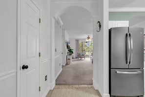 A hallway with white walls, a door, a rug, a chair, and a large refrigerator. - Barefoot Landing Condo Pool & Golf View (North Myrtle Beach)