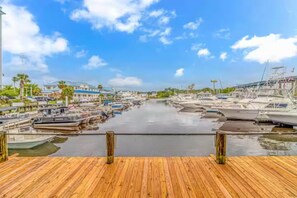 A marina with boats docked, a wooden deck, and buildings in the background. - Waterfront Condo Harbourgate Marina Views (North Myrtle Beach)