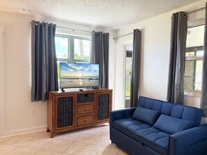 A living room with a television, a blue sofa, and a wooden cabinet with woven doors. - Venice Villas Combo – Sleeps 5 | Poolside (Venice)