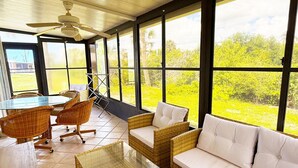 A sunlit room with a glass table, wicker furniture, and large windows offering a view of greenery. - Venice Villas Combo – Sleeps 5 - Poolside (Venice)