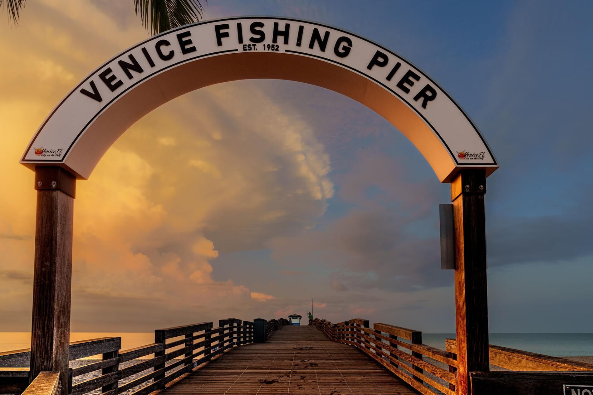 A wooden pier with a sign reading 'Venice Fishing Pier' and a logo for Venice, FL.