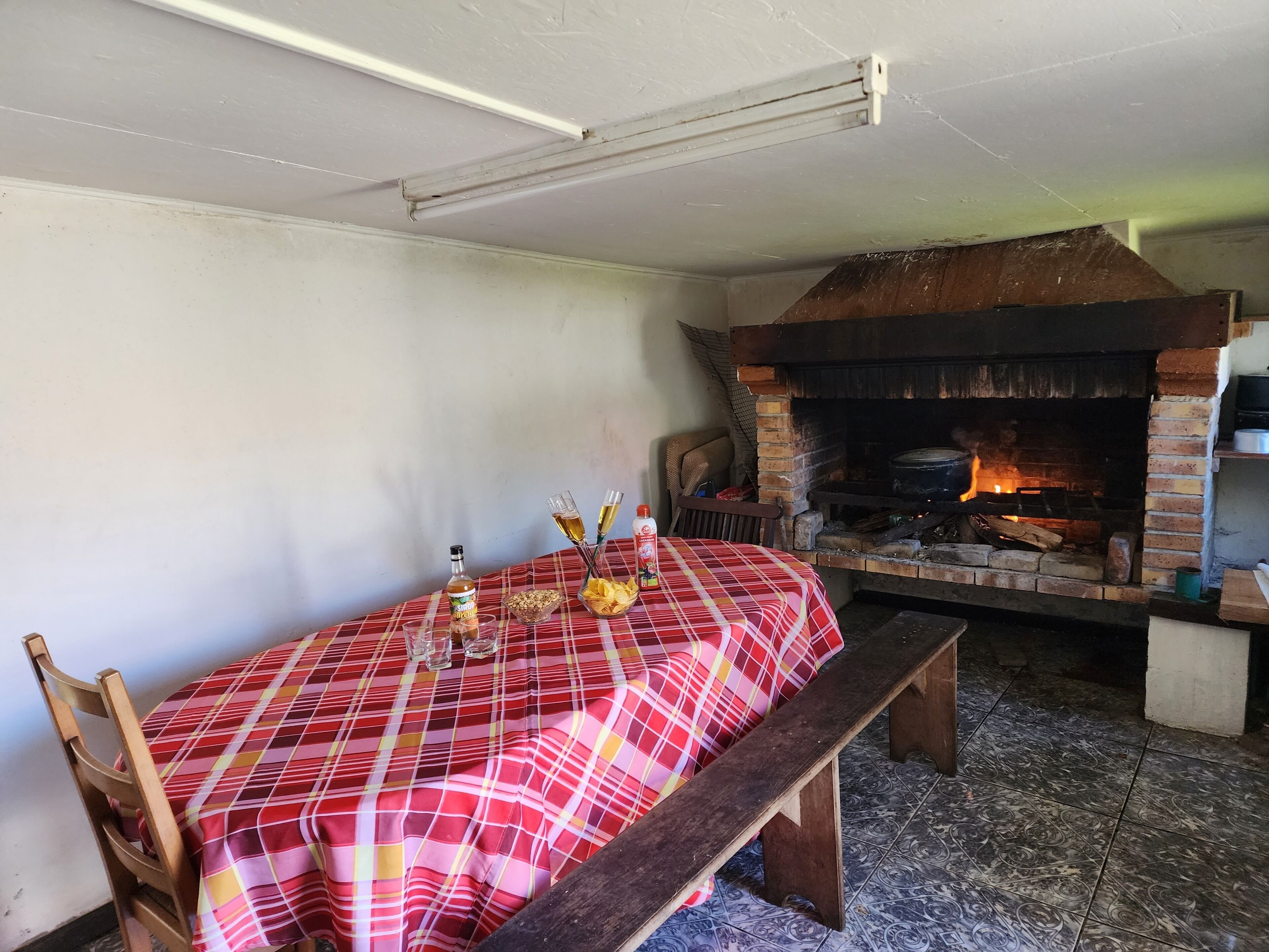 Un coin repas avec une table dressée pour deux personnes, un banc, une cheminée en briques et un luminaire au plafond.