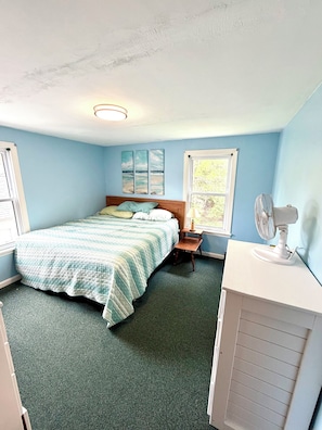 Ein Schlafzimmer mit einem Bett, einem Nachttisch, einem Ventilator und einem Fenster.