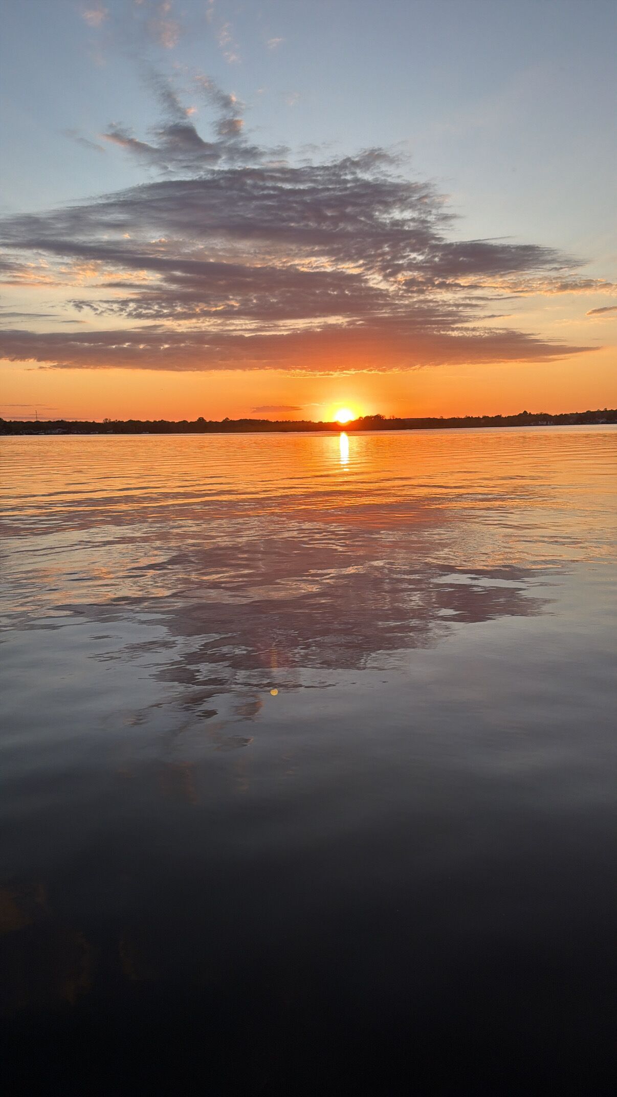 Un coucher de soleil sur une étendue d’eau calme, avec la silhouette d’une côte lointaine.