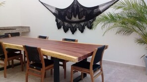 A dining area with a wooden table and chairs, a macrame wall hanging, and a potted plant. - Aura Jungle Oasis (Tulum)