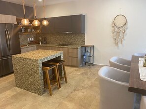 Eine moderne Küche mit Granit-Arbeitsplatten, Holzstühlen, einem Wasserspender und einem Traumfänger an der Wand.