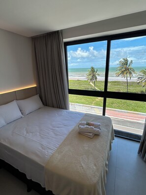 Habitación de hotel con una cama grande, vista a la playa y una ventana con cortinas.