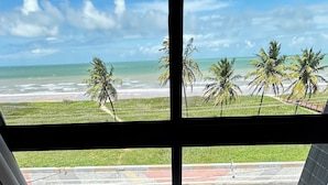 A room with a view of the beach, a bed, and a window with blinds. - Melhores Flats - Exclusividade vista mar (Cabedelo)