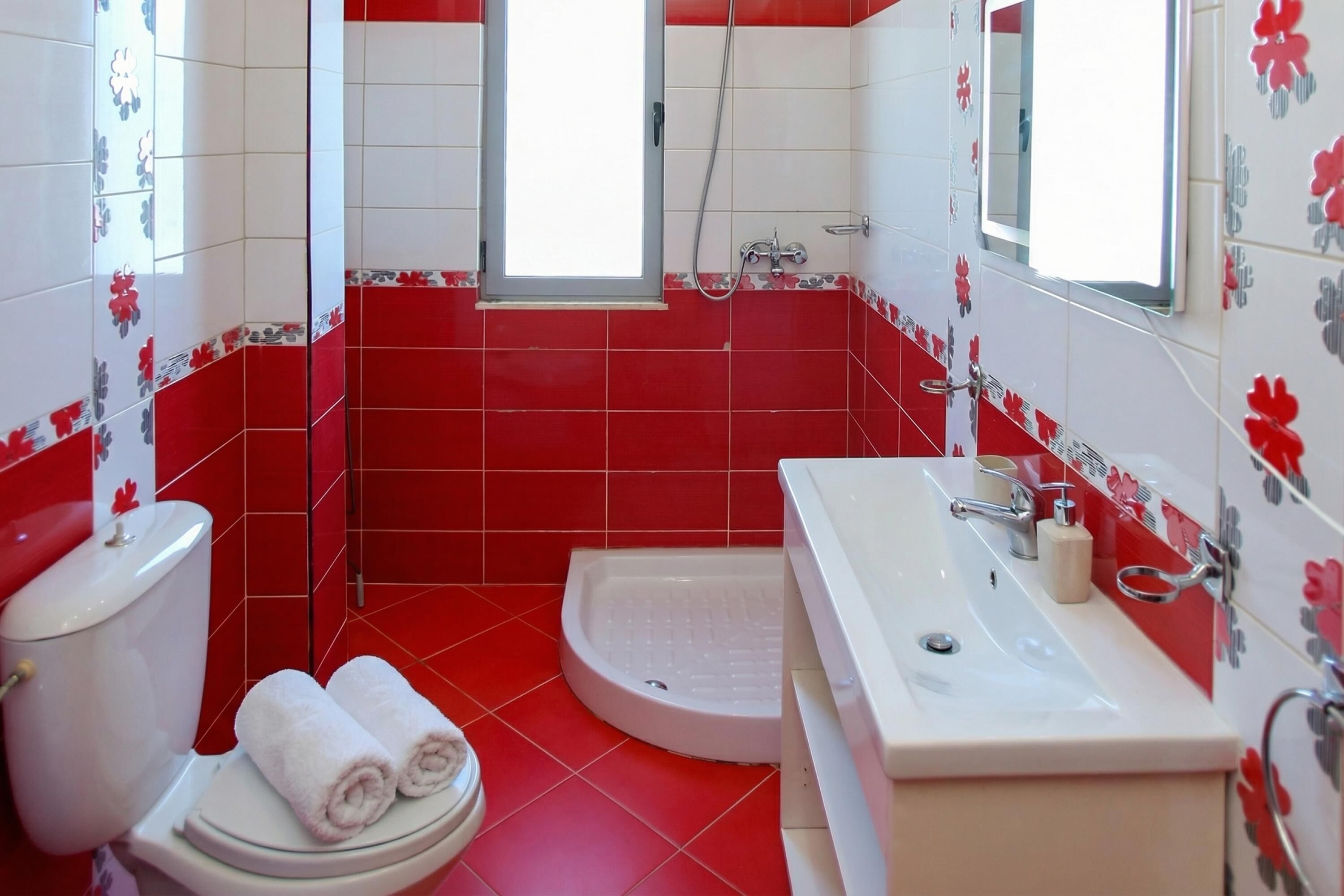 A bathroom with red and white tiles, a toilet, a sink, and a shower.