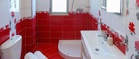 A bathroom with red and white tiles, a toilet, a sink, and a shower.