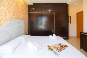 Ein Hotelzimmer mit einem großen Bett, einem Kleiderschrank und einem kleinen Tisch mit einer Zeitschrift und Blumen.