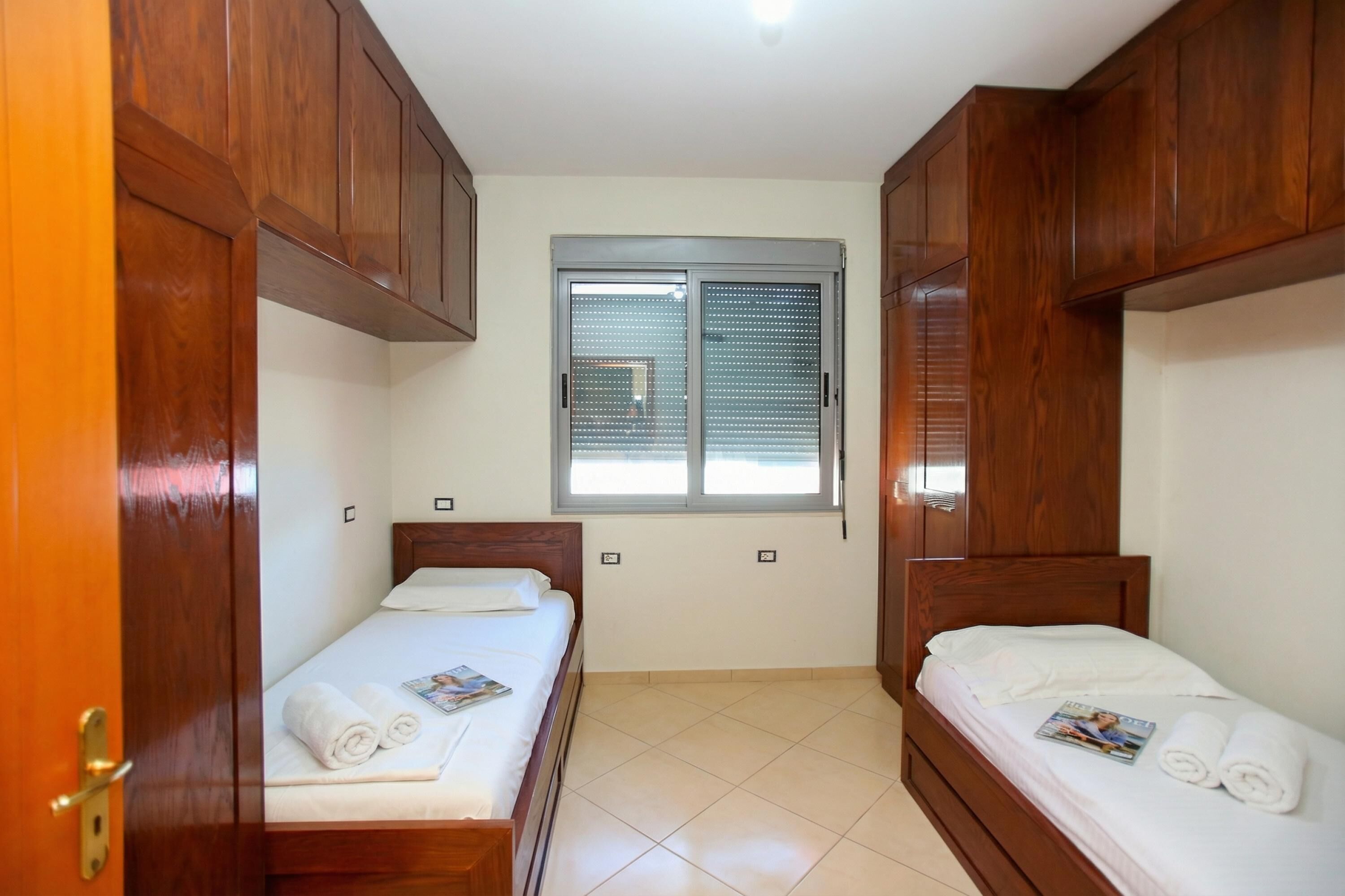 A room with two wooden beds, a window with blinds, and a door.