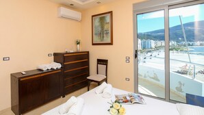 A hotel room with a bed, a dresser, a chair, a painting, and a balcony with a city view. - Holiday Apartment Central & Sea View, Vlore, Albania (Vlore)