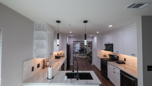 A modern kitchen with white cabinetry, a central island with a sink, a black faucet, and a stainless steel range hood. - Completely Remodeled, Perfect for the World Cup (Dallas)