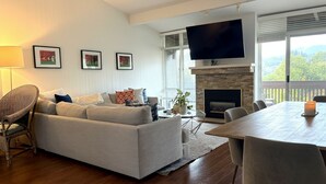 A living room with a sofa, a dining table, a TV mounted above a fireplace, and framed pictures on the wall. - Perfectly located 2-bedroom townhome at The Quail (Carmel)