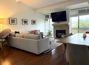 Una sala de estar con un sofá, una mesa de comedor, un televisor sobre la chimenea y cuadros en la pared.