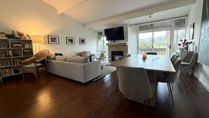A modern living room with a sofa, dining table, and chairs, a fireplace, and a television. - Perfectly located 2-bedroom townhome at The Quail (Carmel)