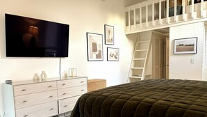 A bedroom with a bed, a TV mounted on the wall, a dresser, a ladder, and framed pictures on the wall. - Perfectly located 2-bedroom townhome at The Quail (Carmel)