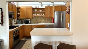 A modern kitchen with wooden cabinets, stainless steel appliances, and a central island. - Perfectly located 2-bedroom townhome at The Quail (Carmel)