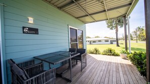 Katettu ulkoalue, jossa on pöytä ja tuoleja. Alueella on kyltti, jossa lukee ”The Beach House”, ja näköala avautuu valkoiseen rakennukseen ja taustalla näkyviin palmuihin.