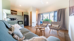 A modern living room with a sofa, armchairs, a coffee table, and a kitchen area with a refrigerator and microwave.