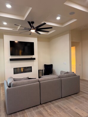 A modern living room with a sectional sofa, a flat-screen TV, a ceiling fan, recessed lighting, and a fireplace. - New Private Desert Escape, Mtn Views with AC in sunny Tucson (Tucson)